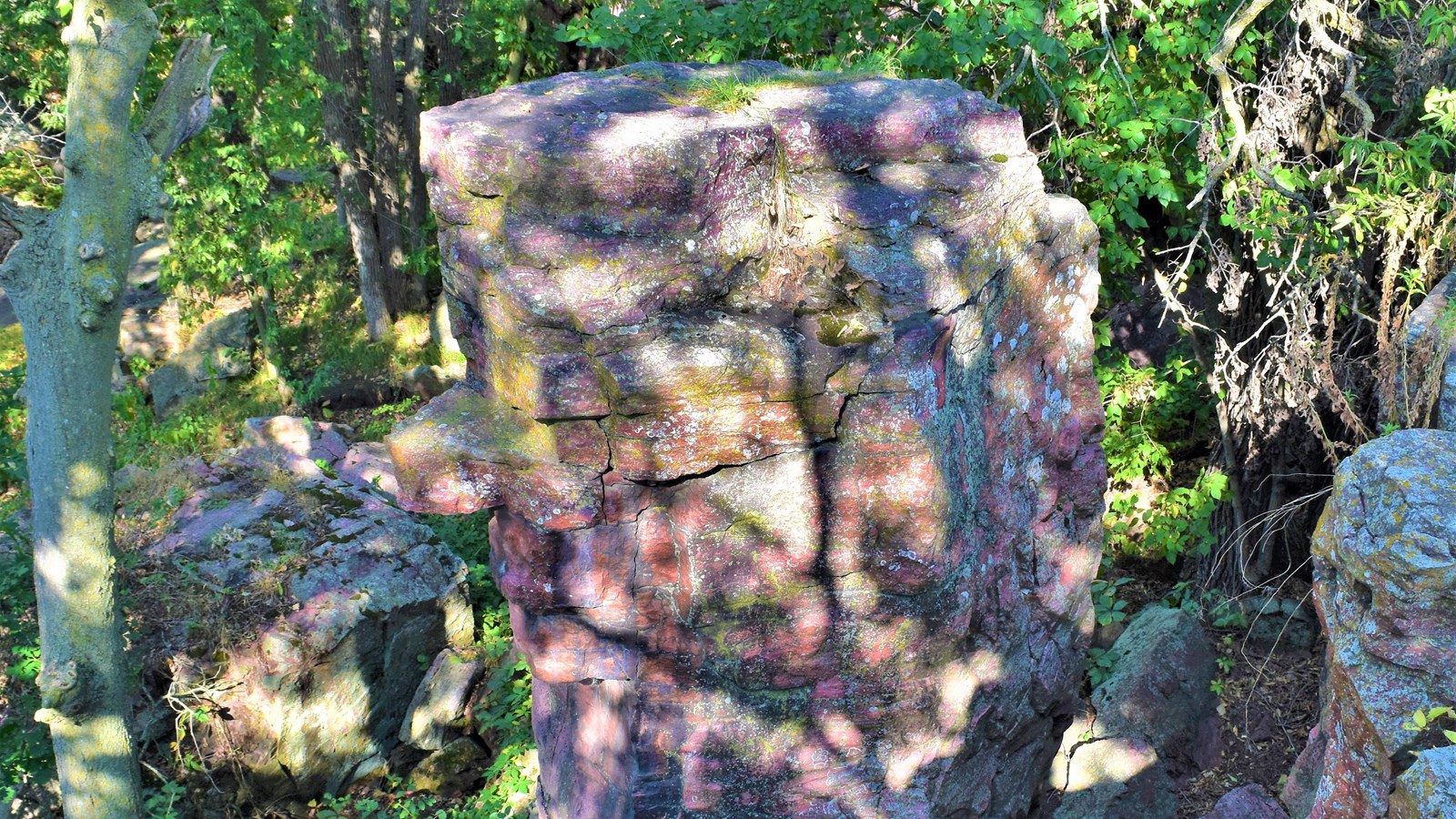 A stone pillar standing 12 feet from a cliff edge surrounded by trees