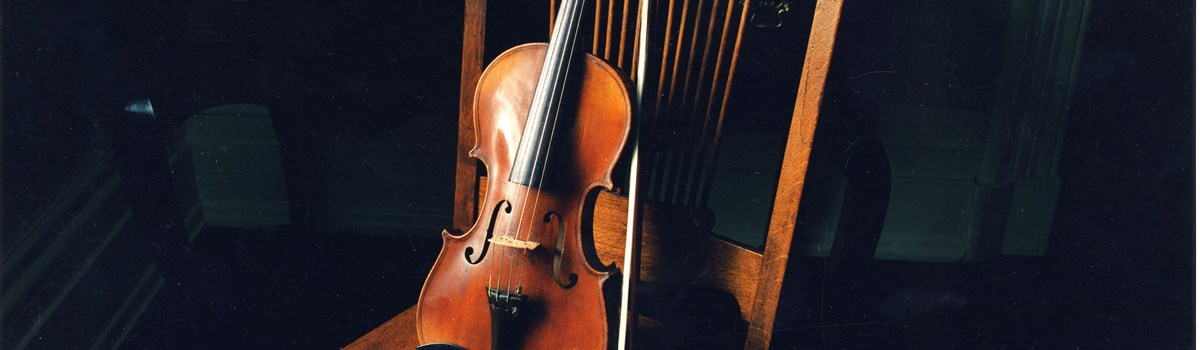 Violin and bow rests against wooden chair.