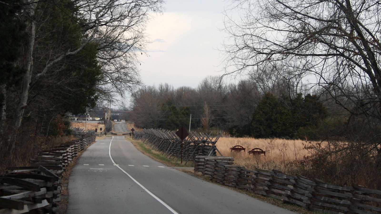 A road flanked by snake rail fence with woods to the left and fields to the right.