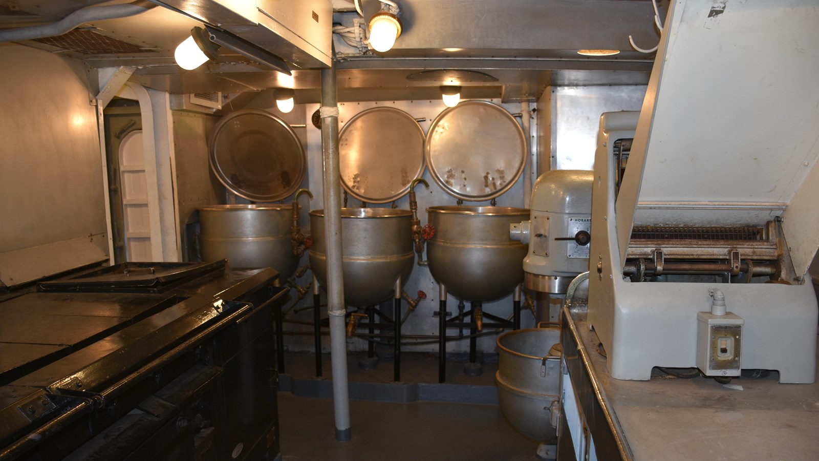 Color photograph of the galley of the USS CASSIN YOUNG with cooking stations and three large pots.