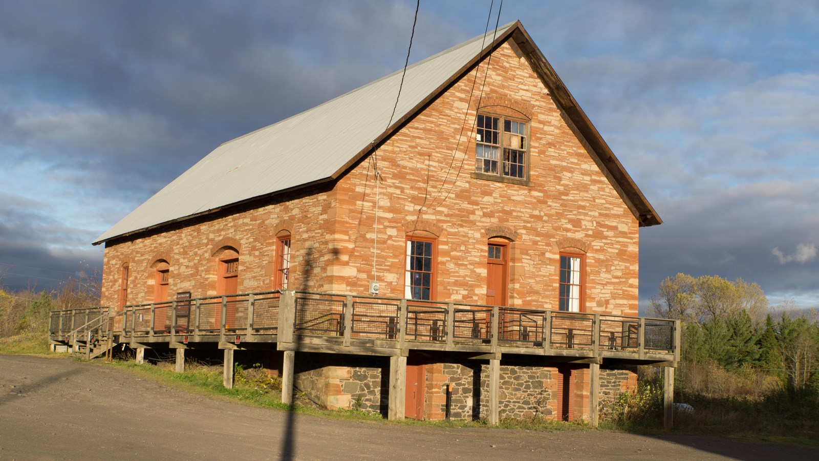 brown and white stone building with a metal grey pitched roof next to a large parking lot 