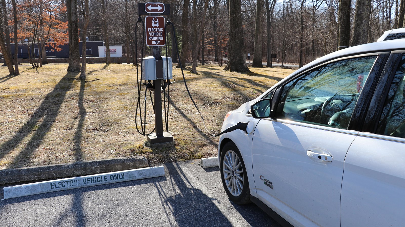 A white electric vehicle plugged into a standing charging station.