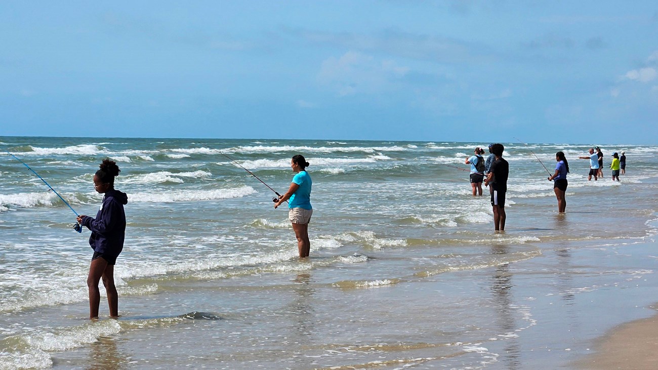 A group of people fish along the beach.