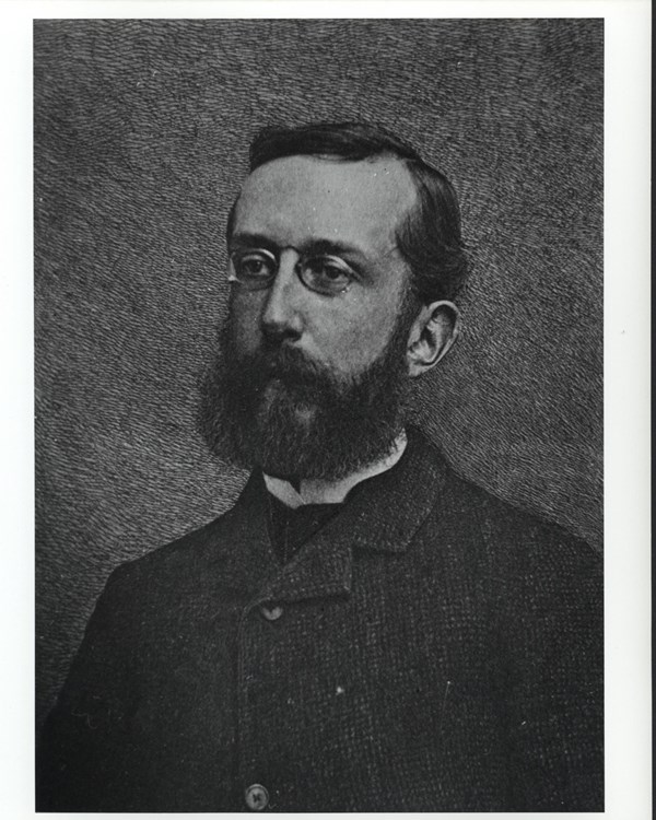 Man wearing dark jacket, with dark hair and thick dark beard poses for portrait. 