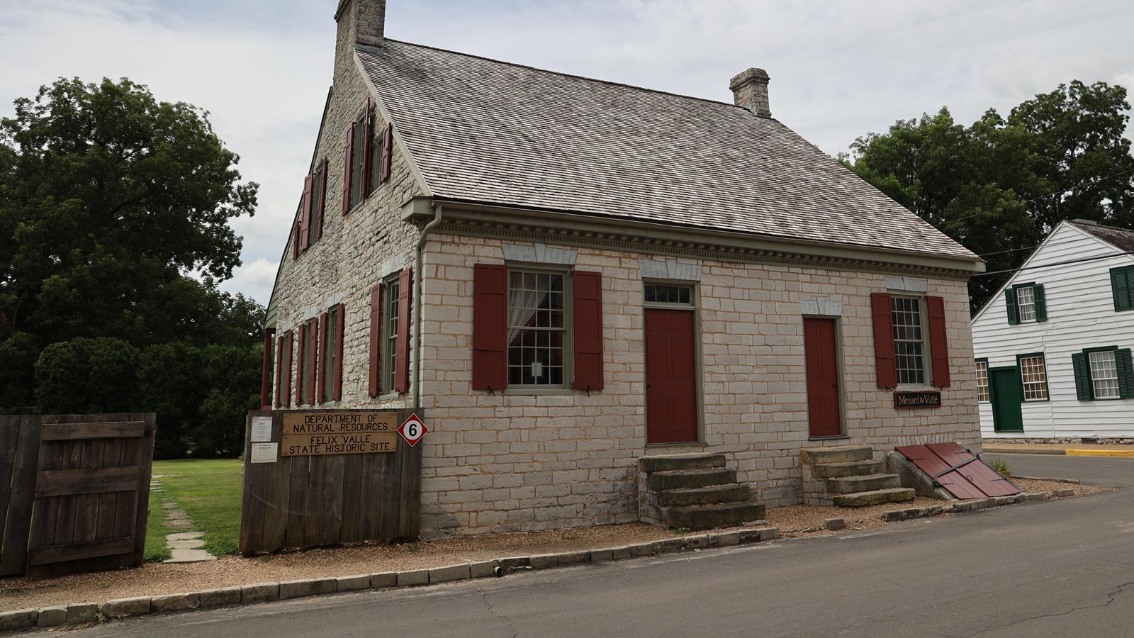 Tan limestone two story house with red shutters and doors.