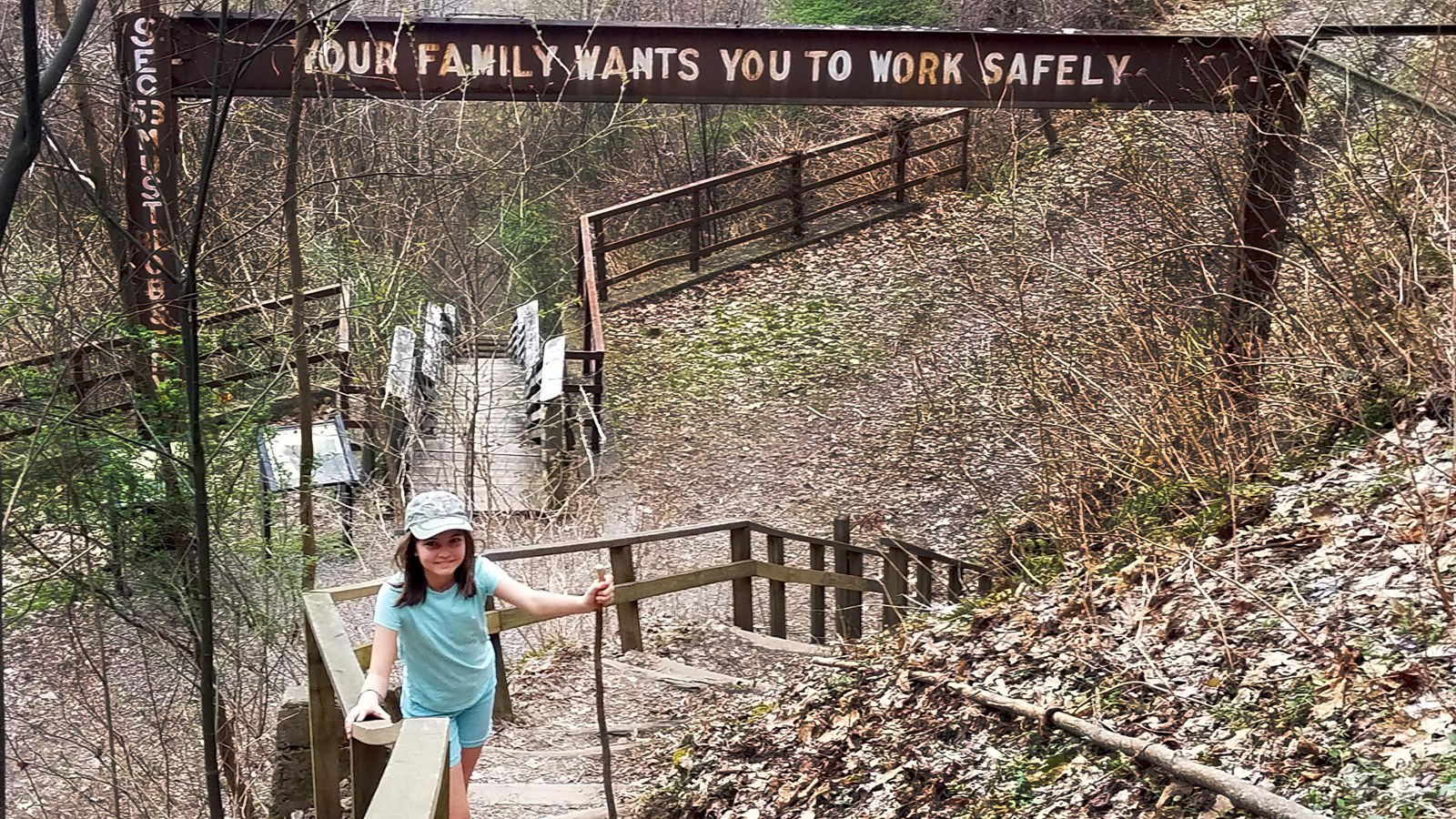 A young hiker on wooden stairs. A sign above her reads, 