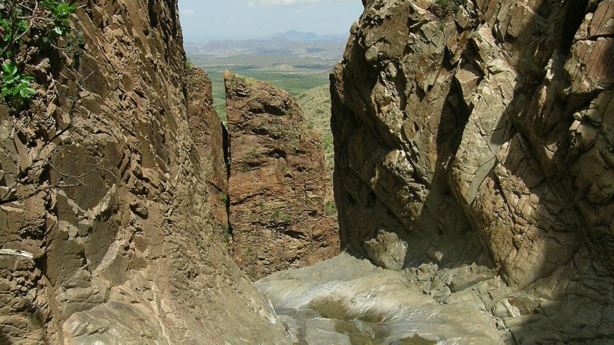 Smooth canyon walls surround a view out to the desert below.