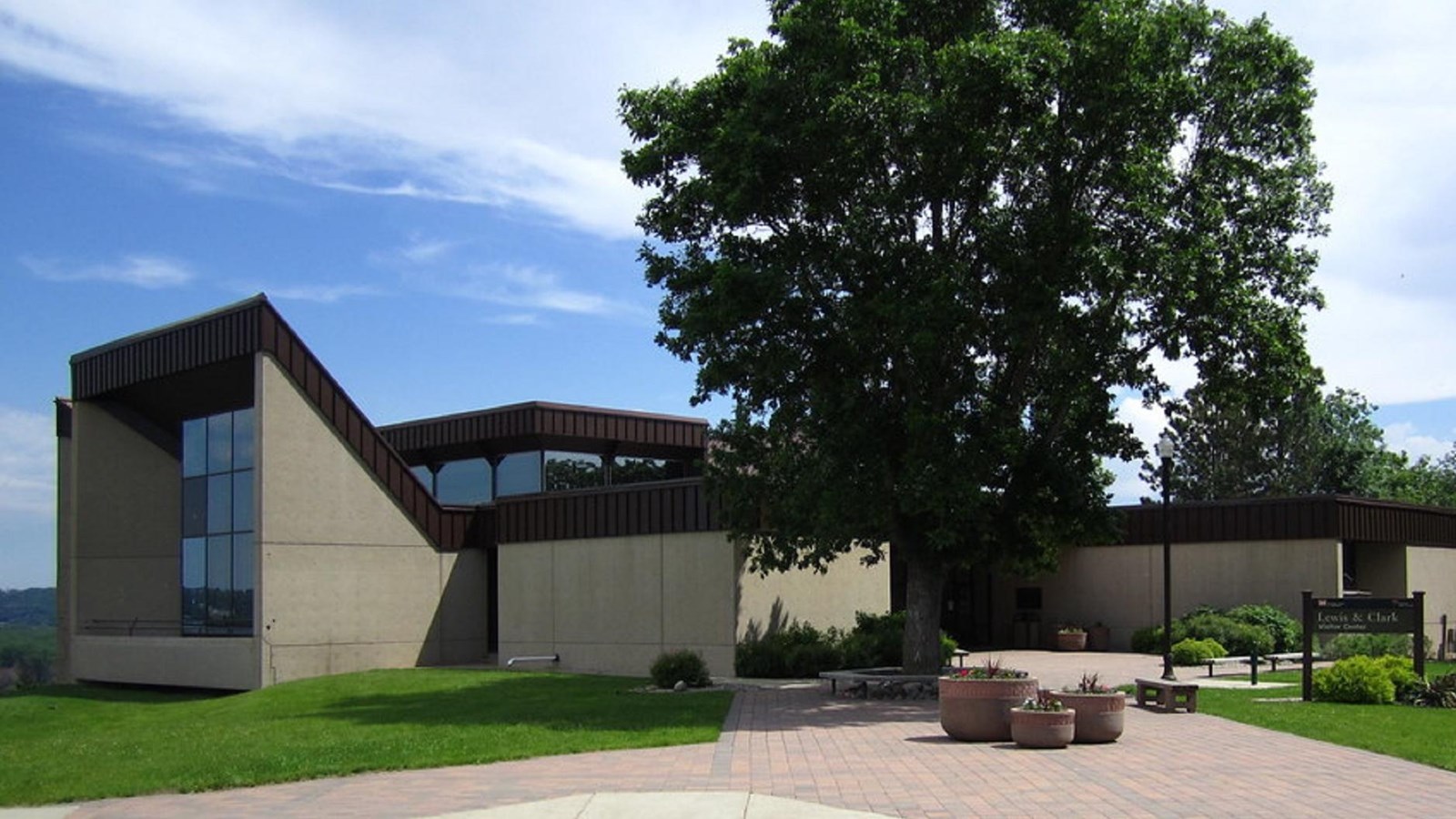 Brick walkway leading towards a beige building with a tree in front of it