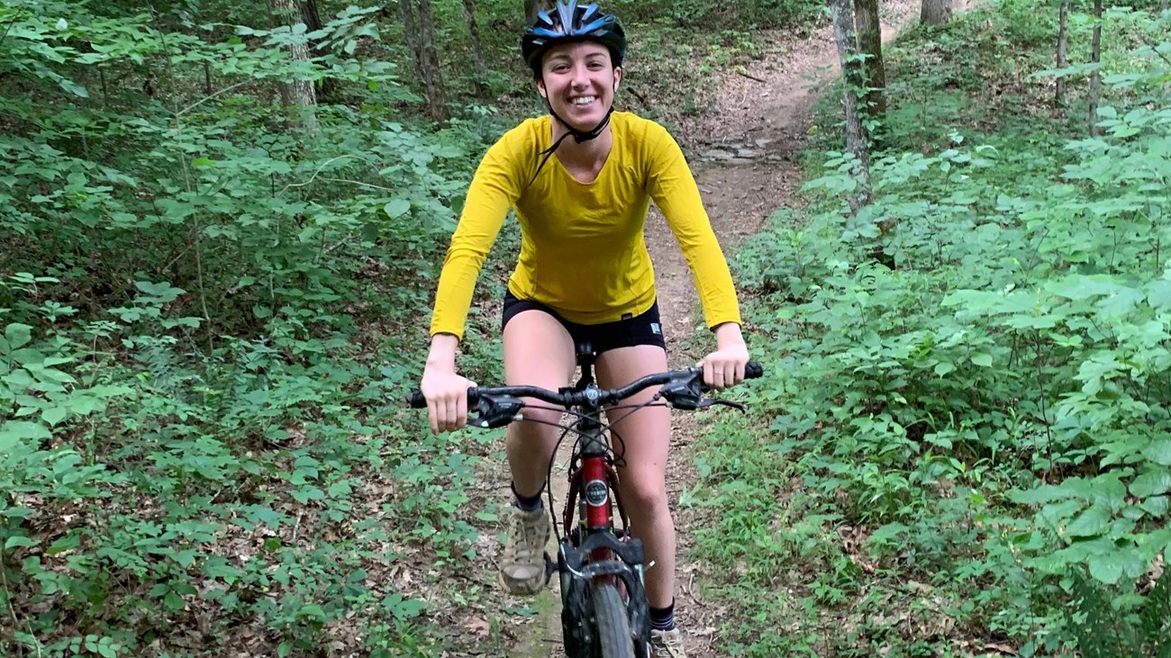 A young woman riding down a narrow trail on a mountain bike.