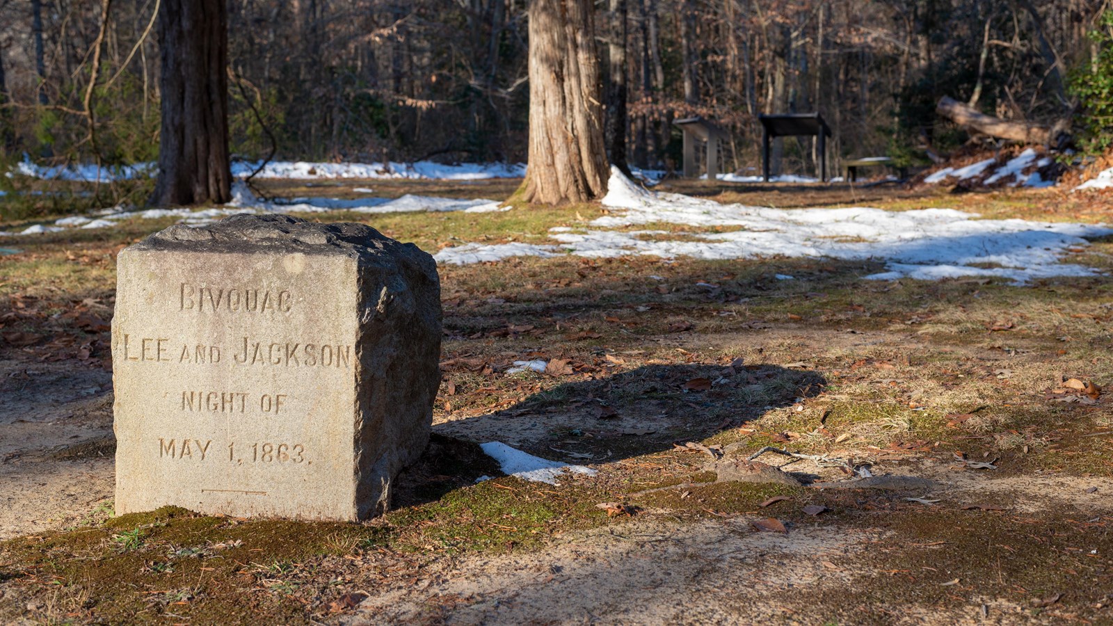 A foot-tall rectangular stone marker in front of an open space surrounded by trees.