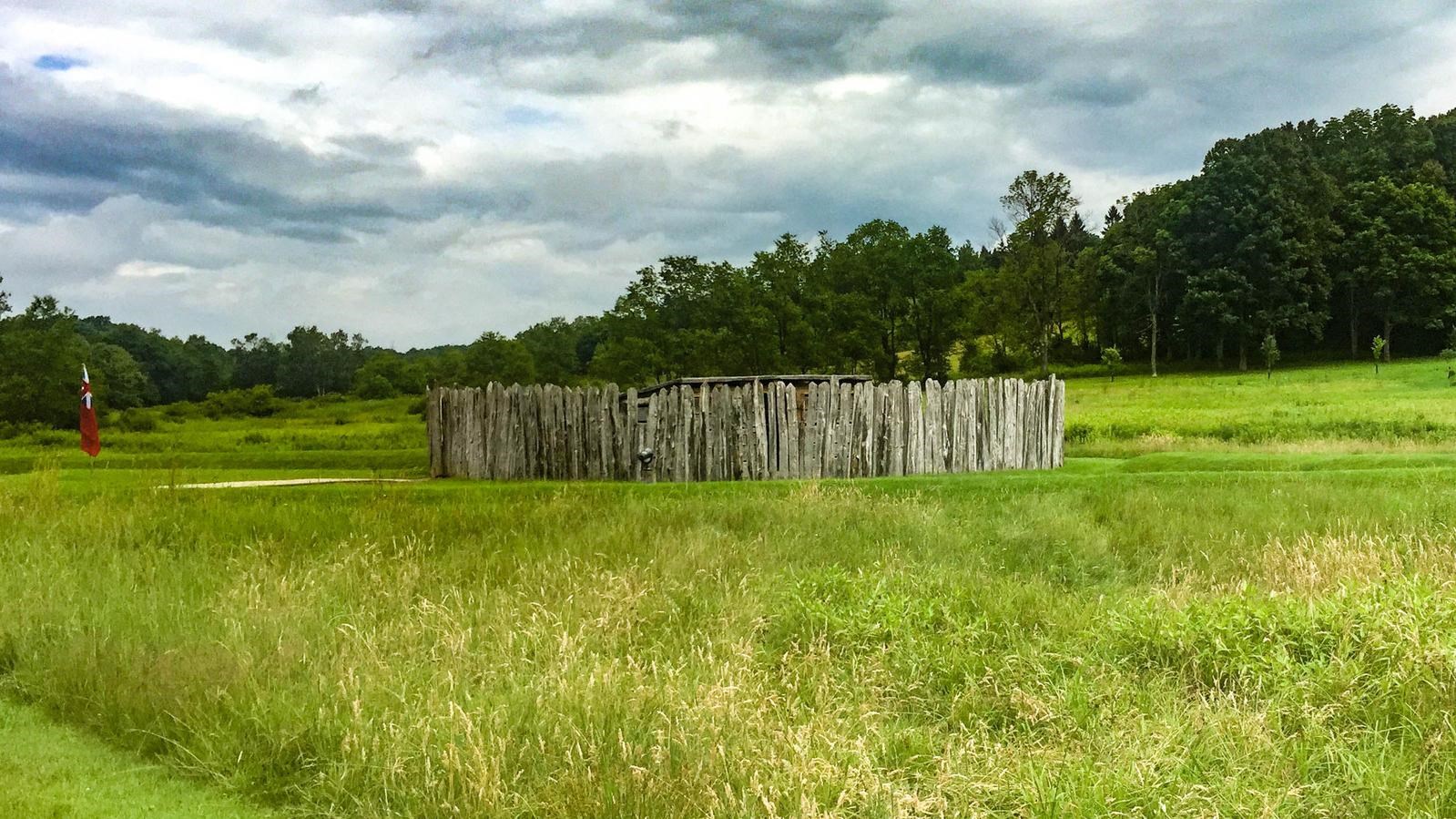 A wooden stockade and earthworks in a meadow.