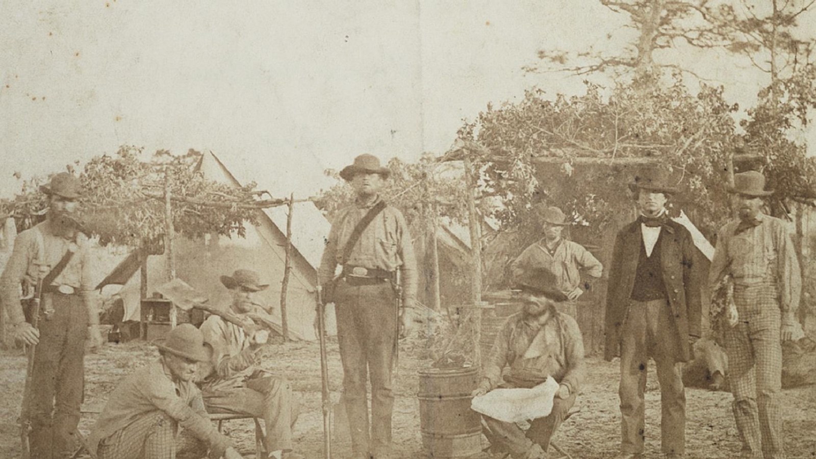 Men in a black and white photograph pose in camp