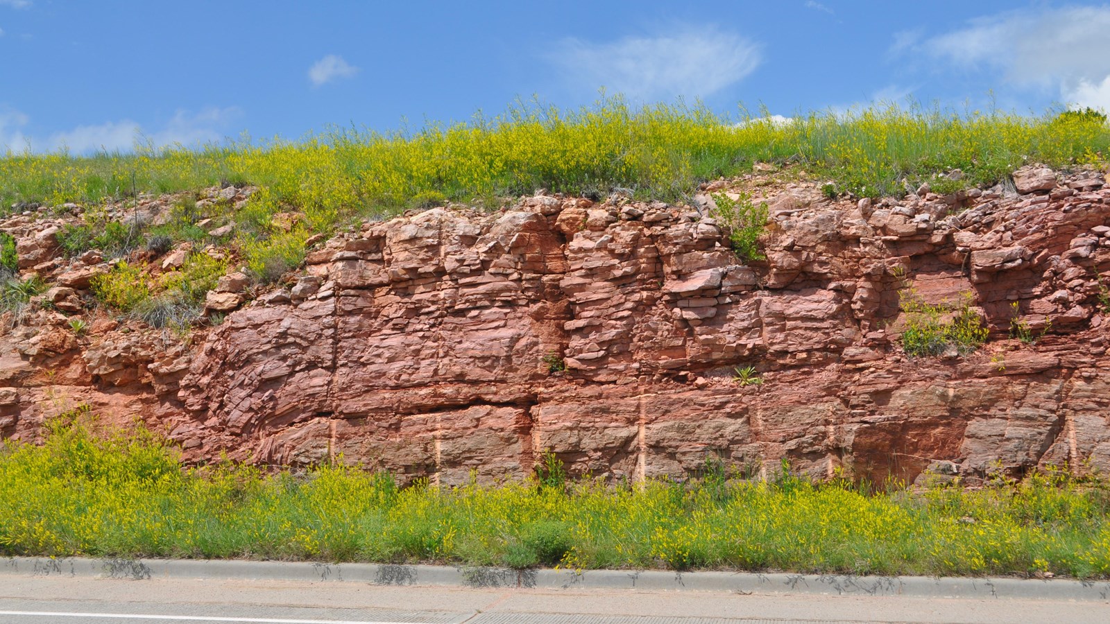 a layer of reddish stone made of many thinner layers next to a paved road