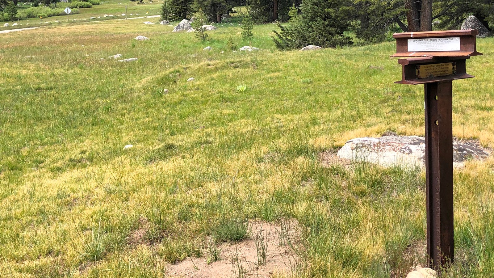 A marker made of railroad rail topped by two pieces of rail with silver plaques, illegible.