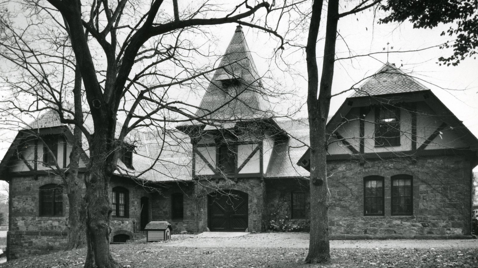 A black and white image of the Carriage House.  A stone building with large barn doors in front.