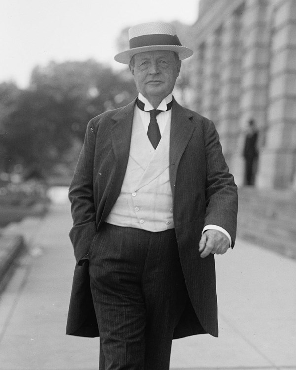 A black and white image of a man in a flat topped straw hat walking towards the camera