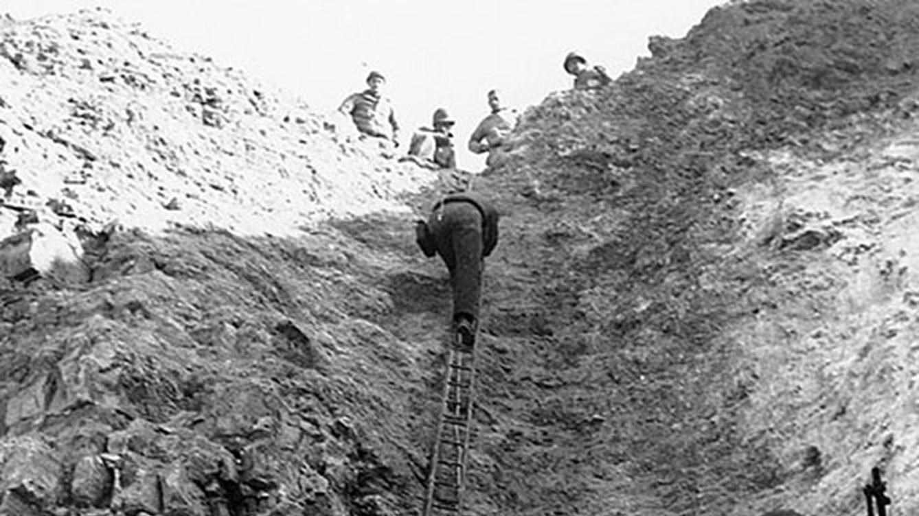 Uniformed man climbing a wooden ladder while other men watch