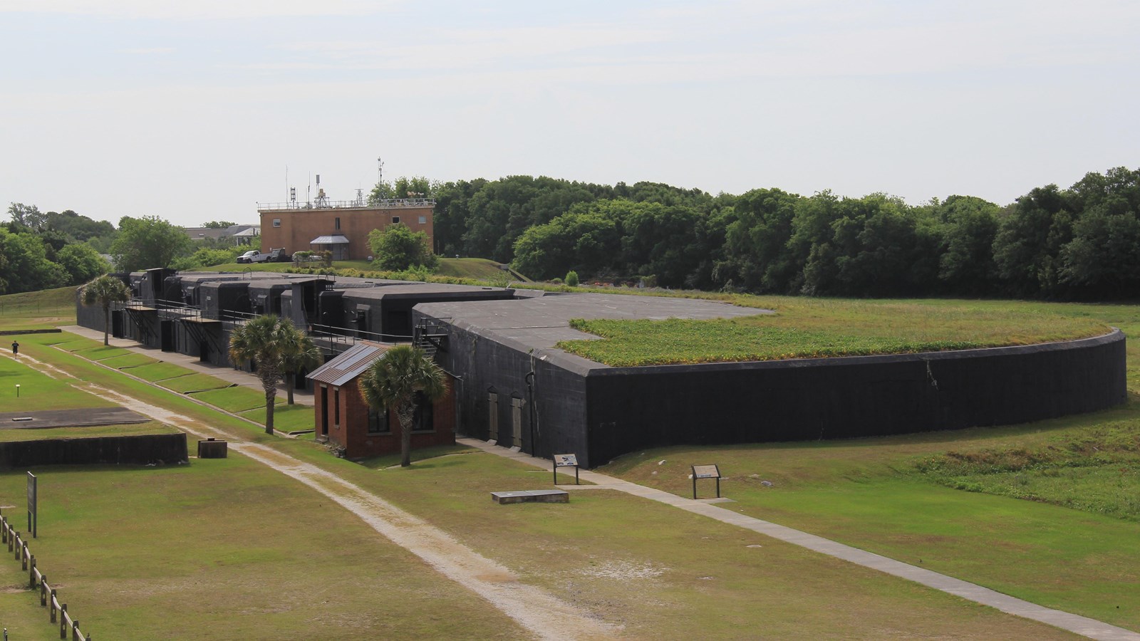 Concrete structure, black in color. Grass field behind it paved sidewalk running along back wall. 