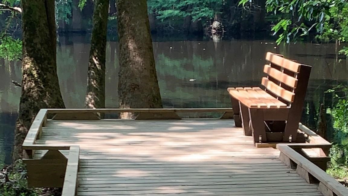 A section of wooden boardwalk trail which overlooks a lake. 
