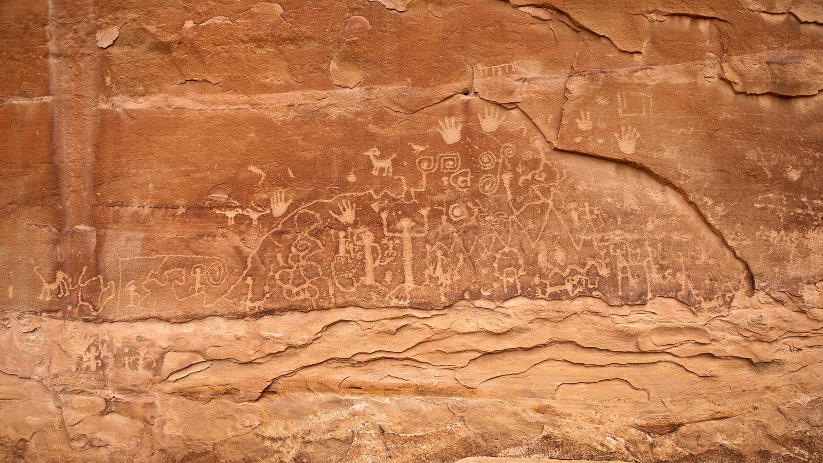 Red-colored sandstone with pecked geographic, animal, and human figures.