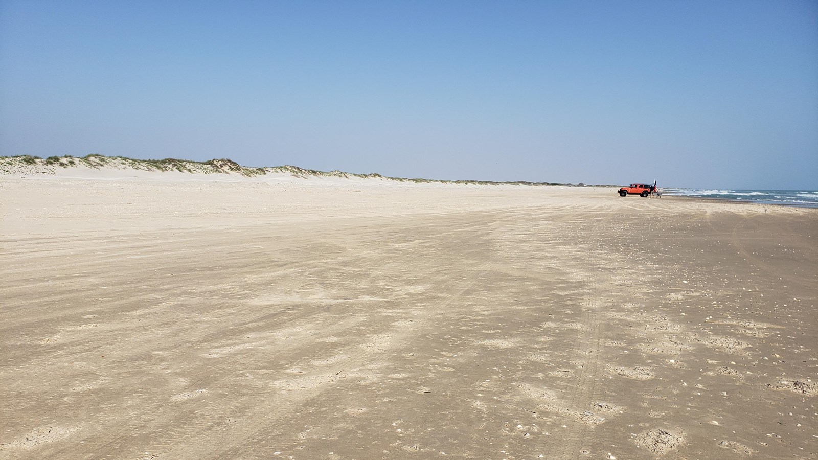 A long sandy beach with a red truck in the distance.