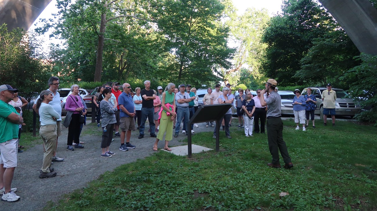 Group of visitors listen to Ranger talking with large cement bridge in background