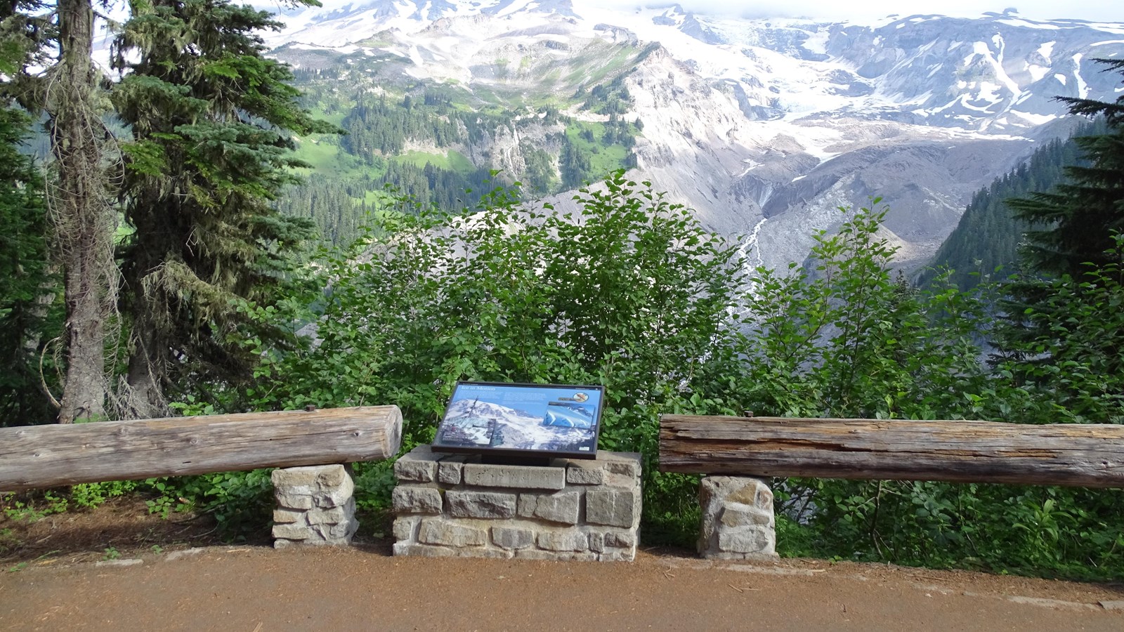 An overlook with a wayside bordered by low log railings. Nisqually Glacier is in the distance.