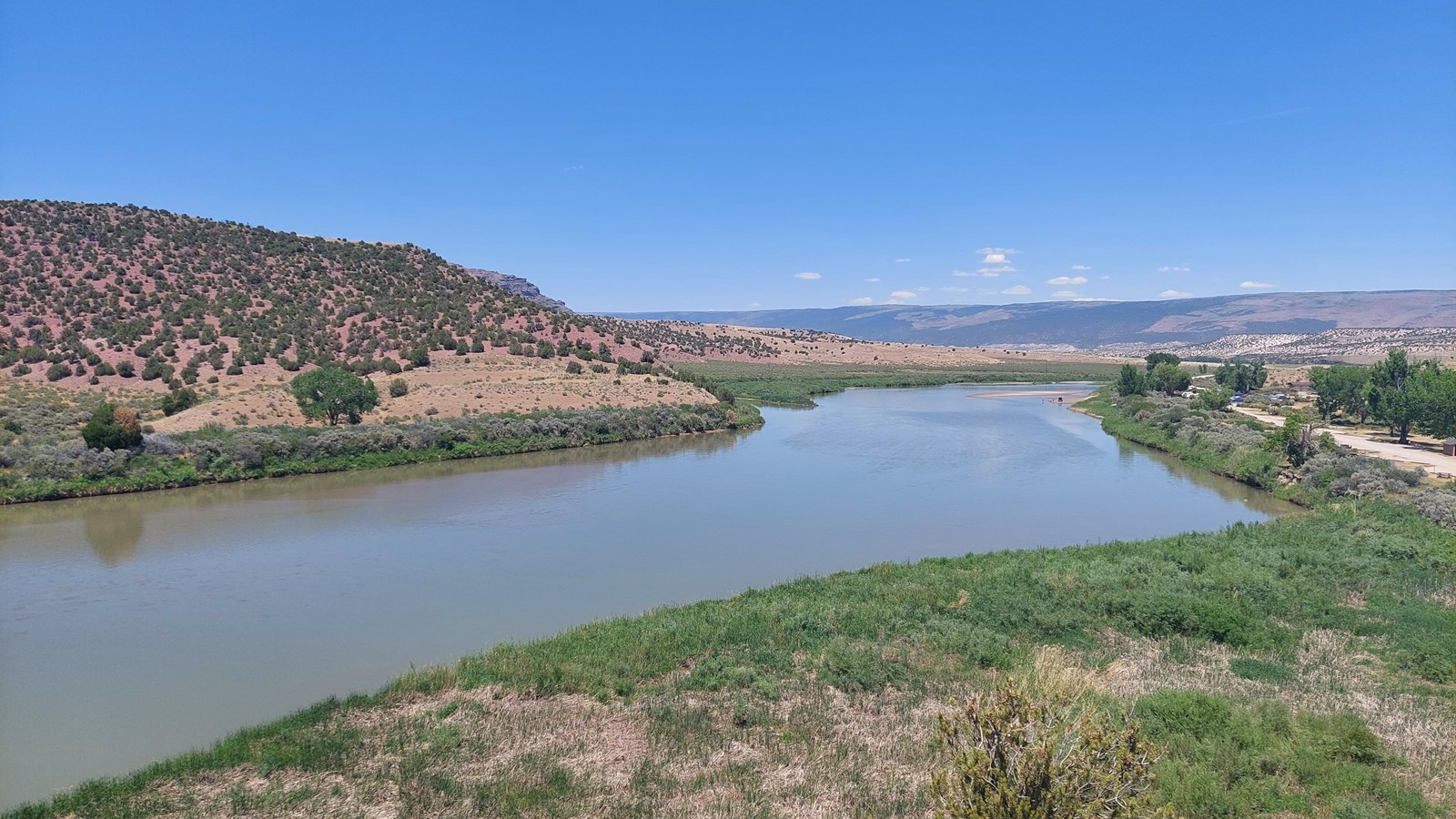 A large greenish-blue river flowing through a desert landscape with greenery along the banks.
