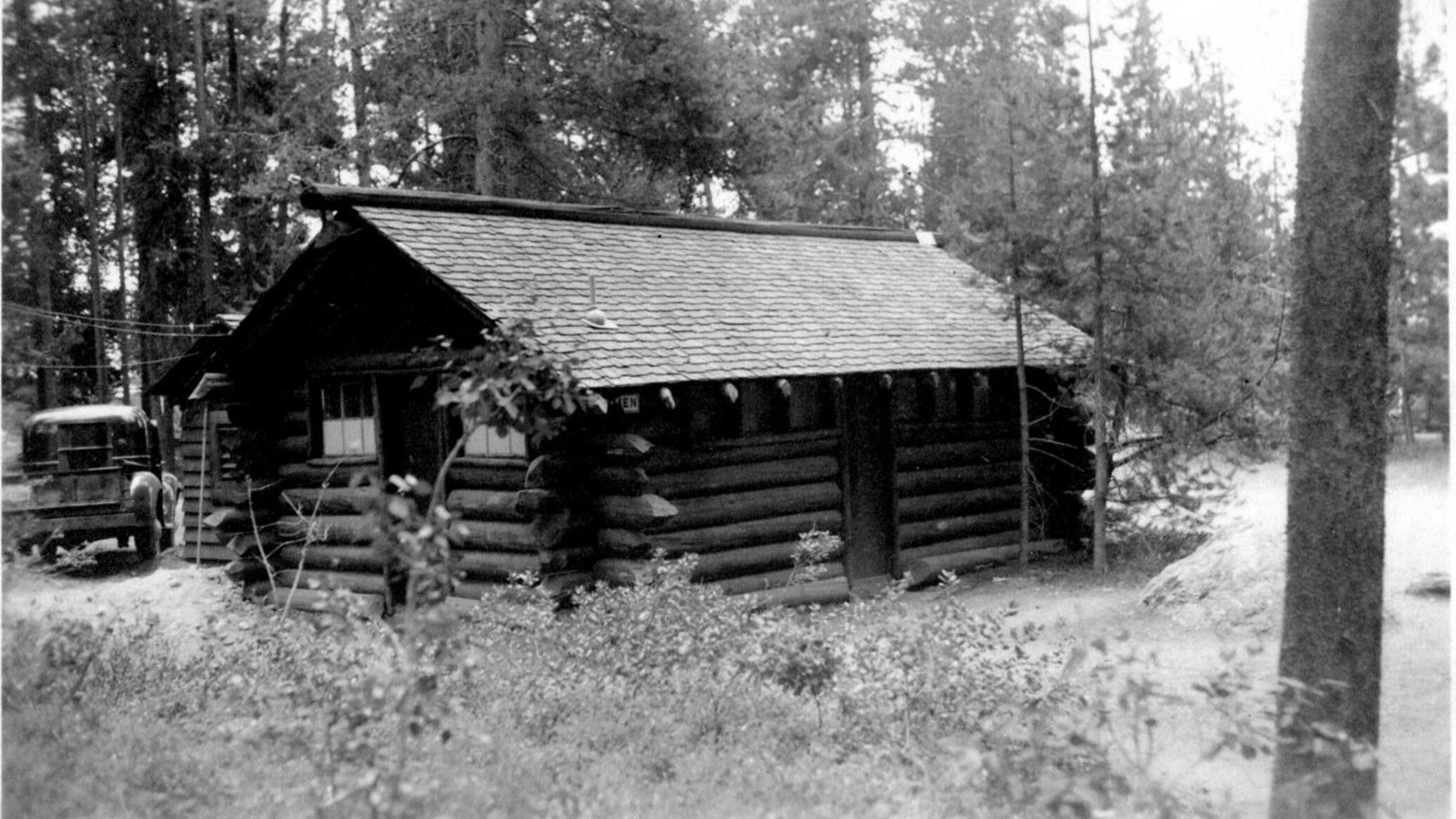 An old black and white photo of the original cabin and an old automobile.