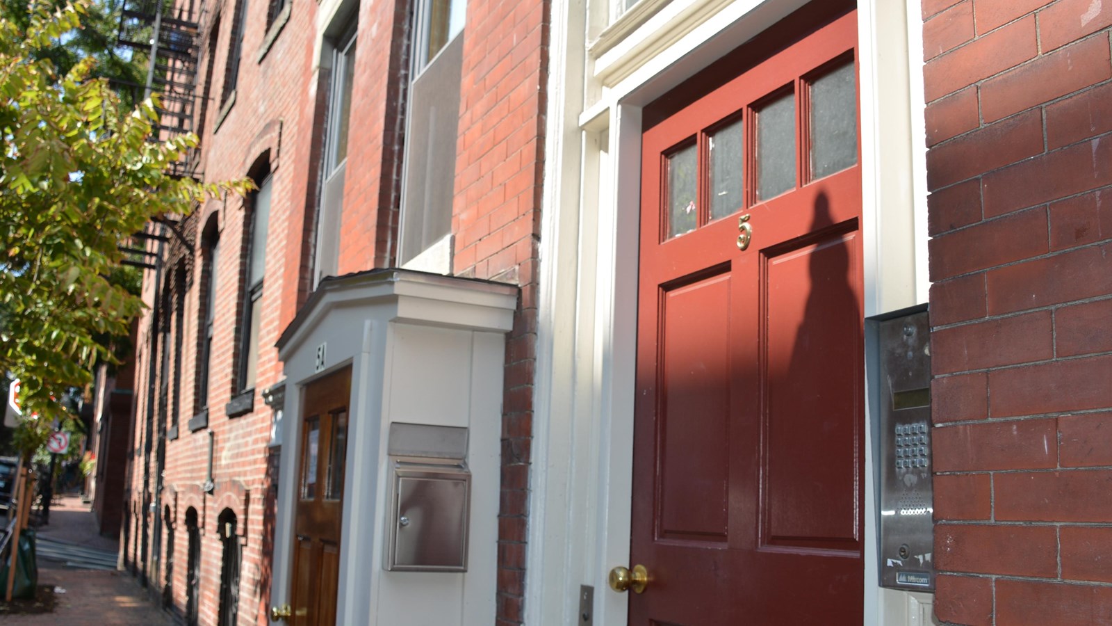An angled view of a red front door of a brownstone. a smaller red door is to its left.