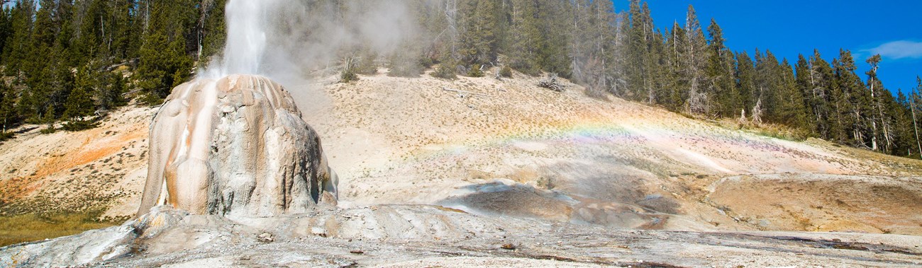 Steam and water erupt from the tan cone of Lone Star Geyser.