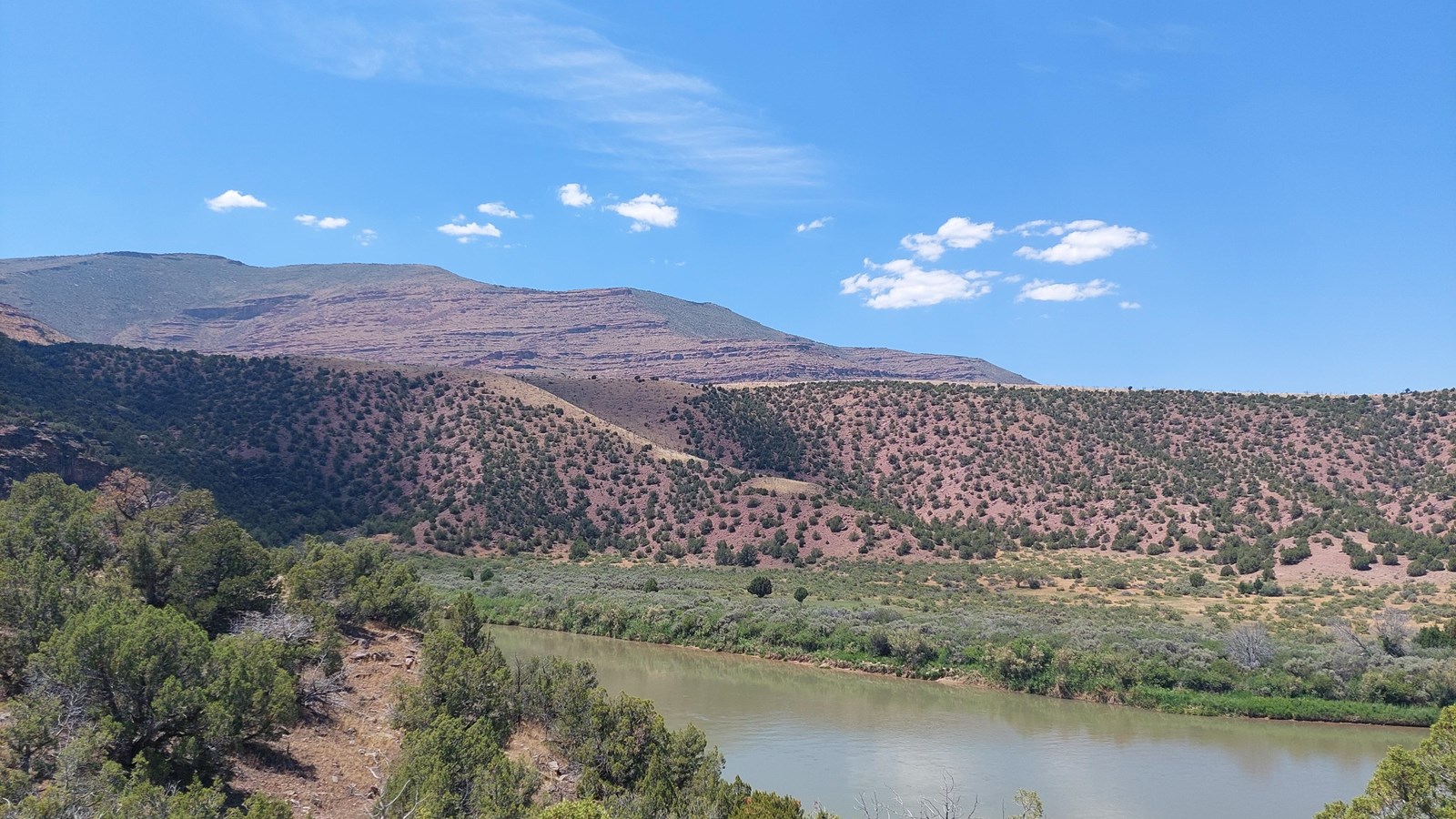 Large reddish hills and mountainsides with a river flowing in front of them.