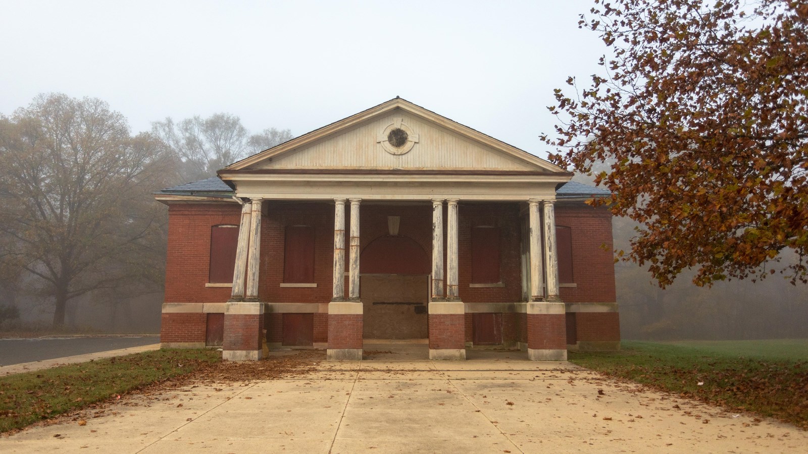 Two story brick building with grey roof and 4 columns in front. Its windows are boarded