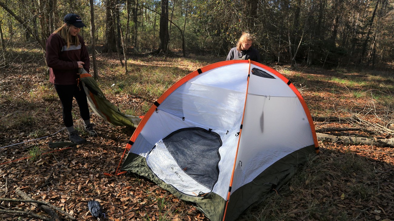 2 people setting up a tent in the woods