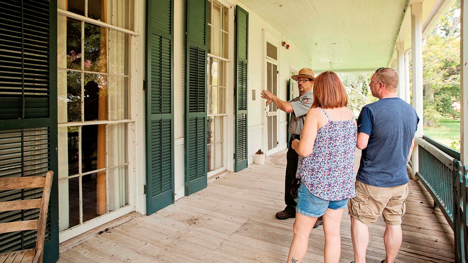 A ranger and two visitors stand on the front gallery (porch) of the Oakland Plantation Main House.