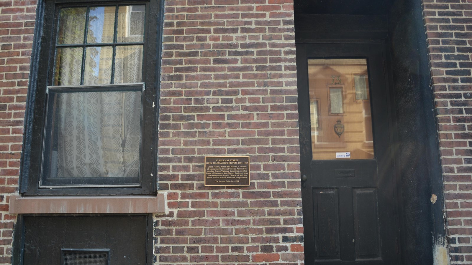 The front of a brownstone with a black door on the right and a historic plaque to it\'s left. 