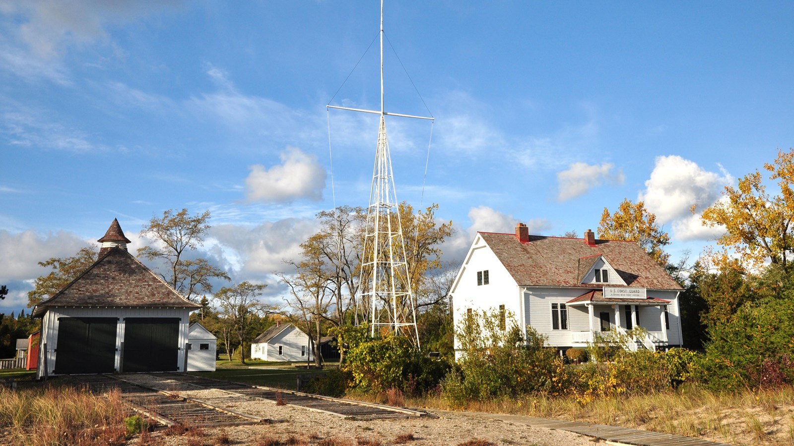 A two doored shingle roof boathouse and 2 story white building with large front porch