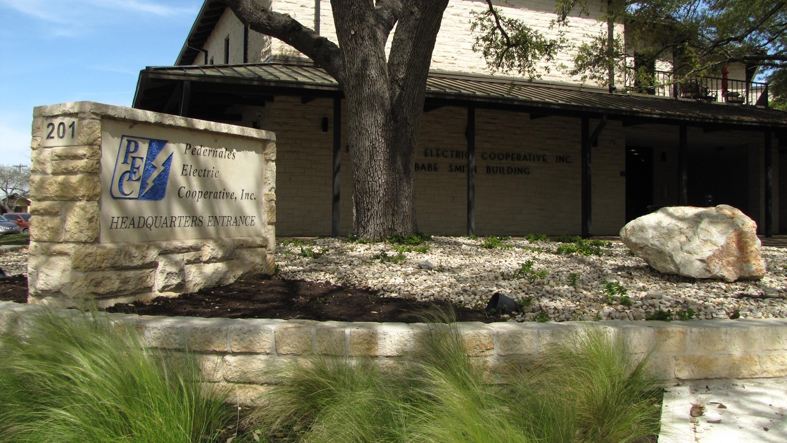 A limestone sign for the Pedernales Electric Cooperative sits in front of the large, two-story headq