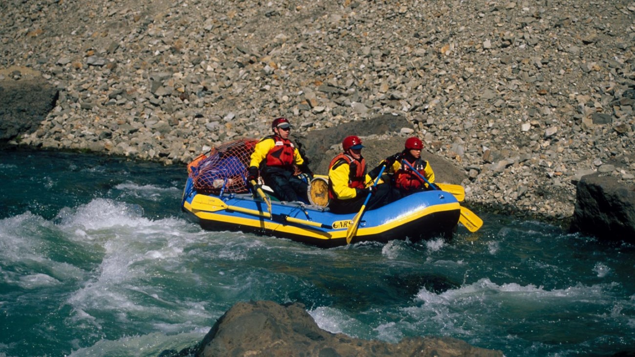 Three people with safety gear in a raft on turquoise and white water