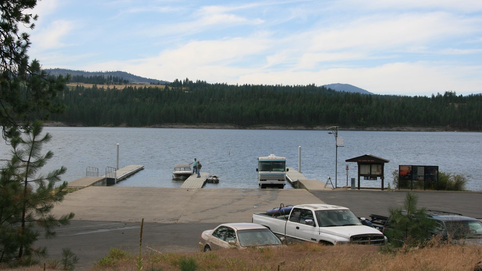 A view of the paved boat launch with 3 docks, the information kiosk to the right, and parking.