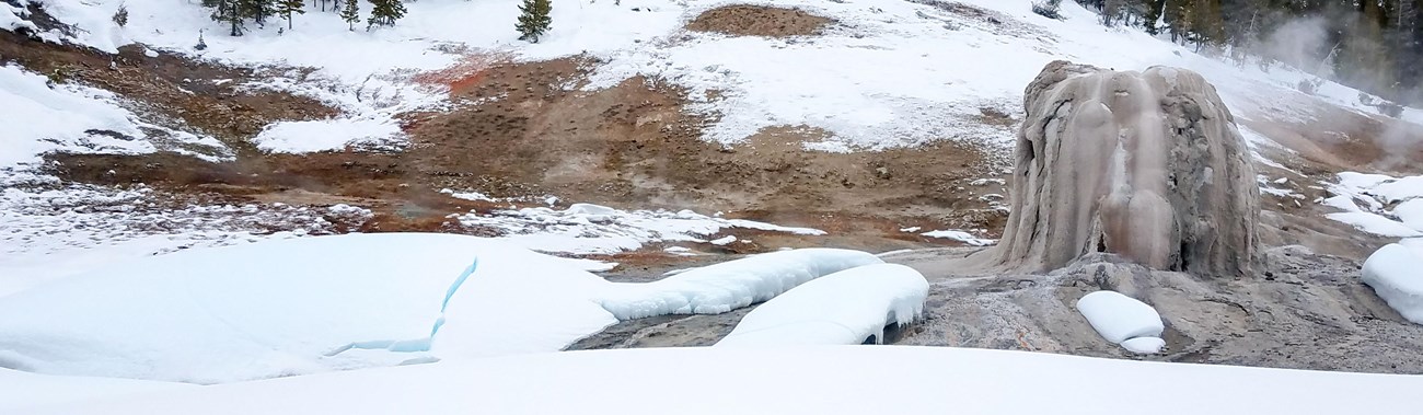 The tan geyserite cone of Lone Star Geyser surrounded by snow.