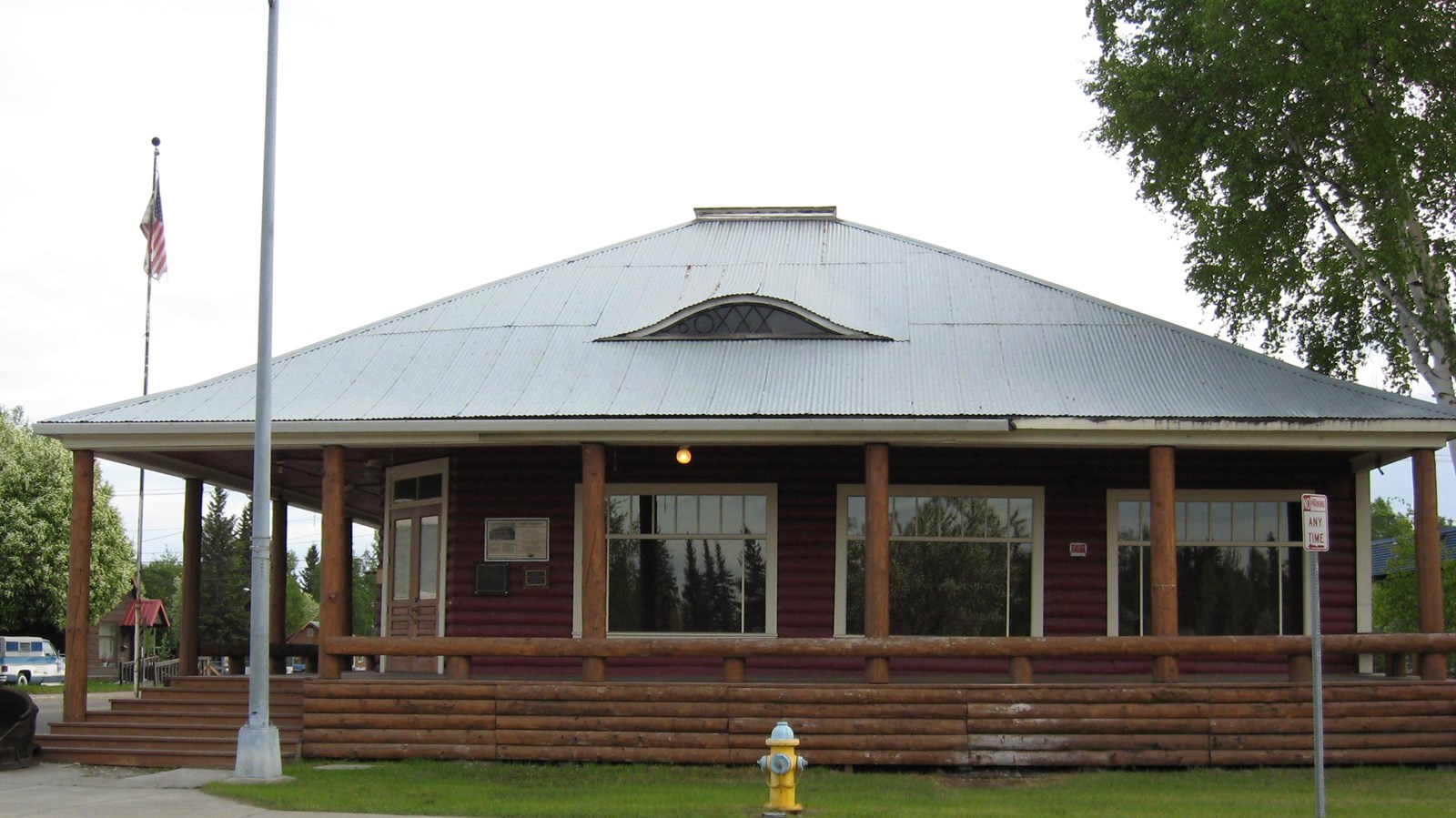 A one story log building with a gray roof and a wrap-around porch with log pillars