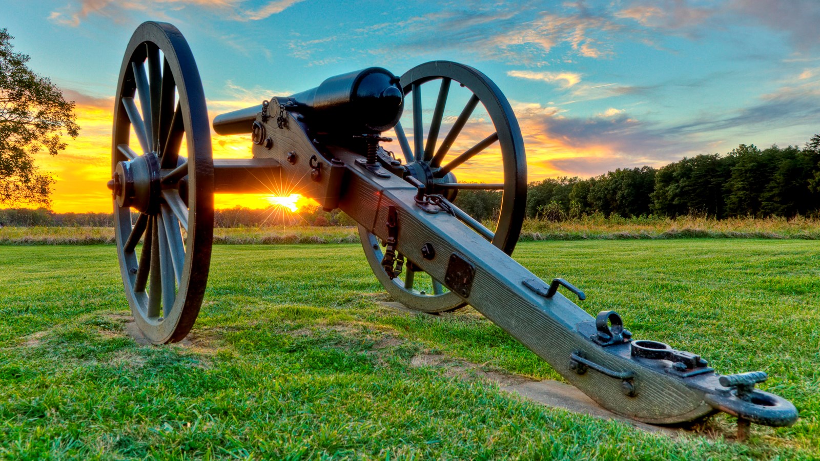 A cannon in a field at sunset.