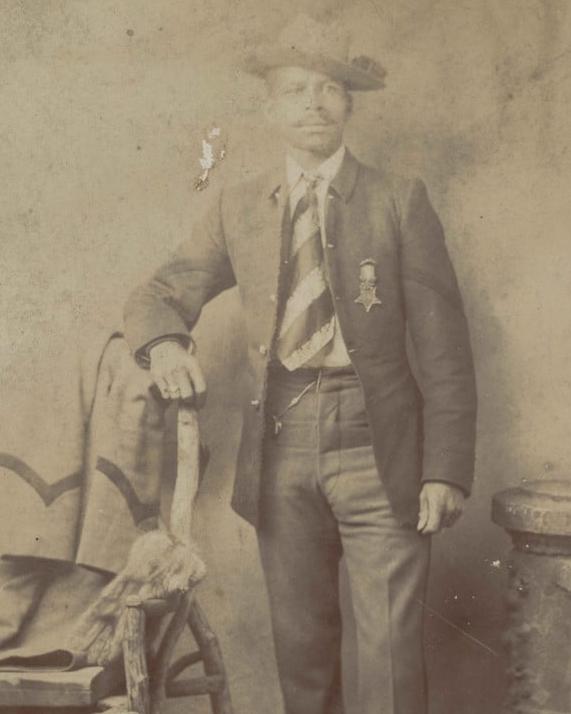 Black male in suit wearing military medal with arm against the top of a chair