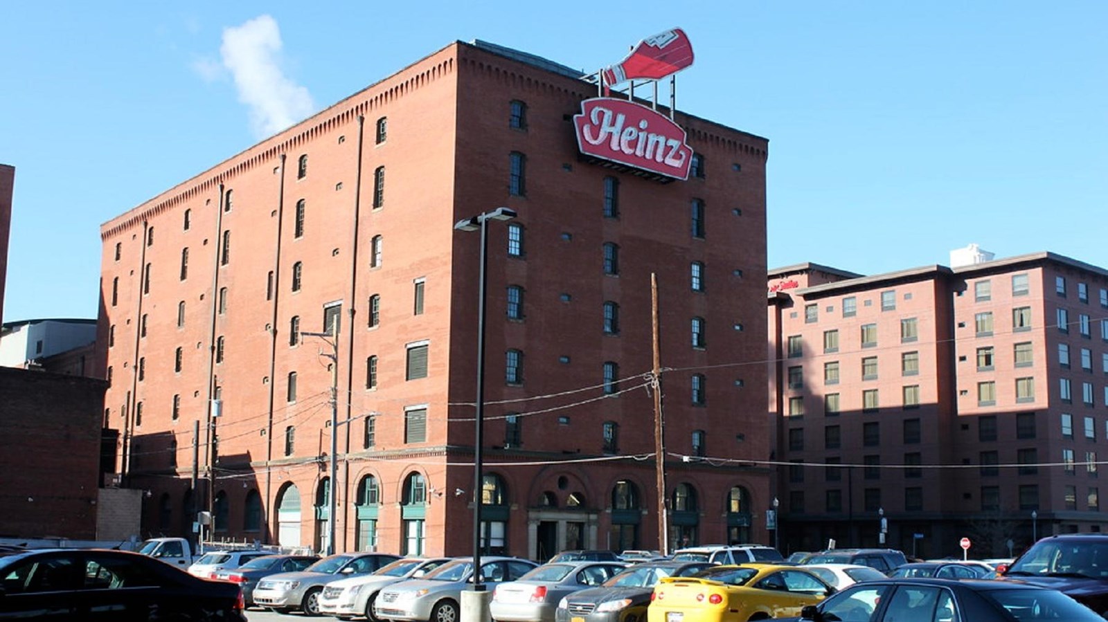 A seven-story rectangular brick factory building with a neon sign of the Heinz ketchup bottle logo