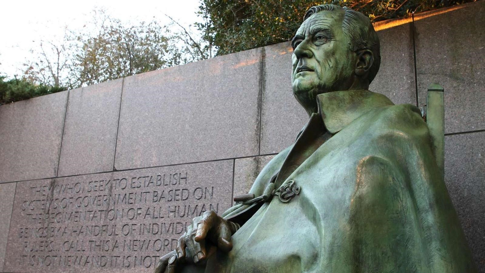 Statue of man (FDR) in front of stone wall with inscription.