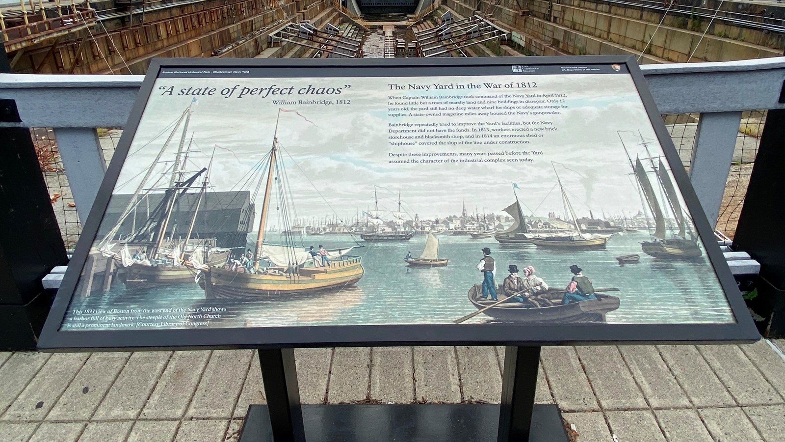 Sign at Charlestown Navy Yard with painting of ships in harbor and words about the war of 1812