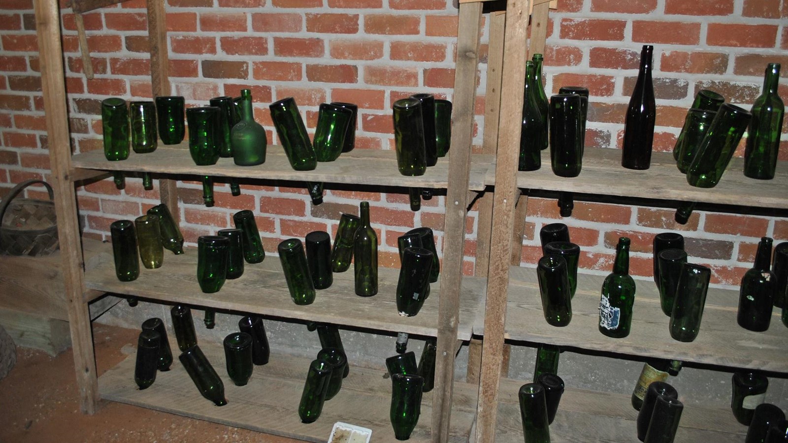Glass bottles stored upside down in wooden racks against a brick wall.