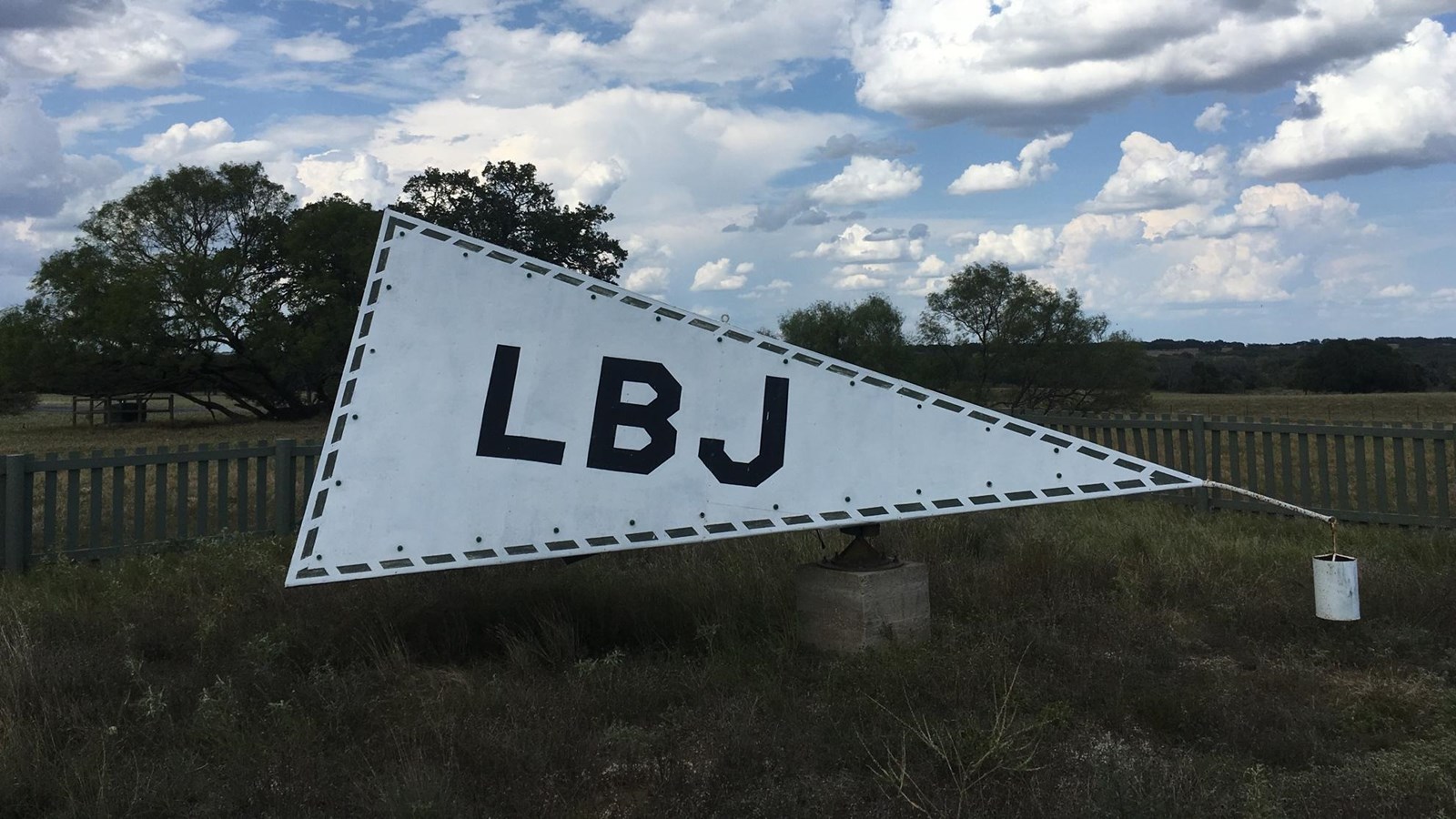 Under white clouds, a gray triangular pyramid sits with dark letters L-B-J on its side.