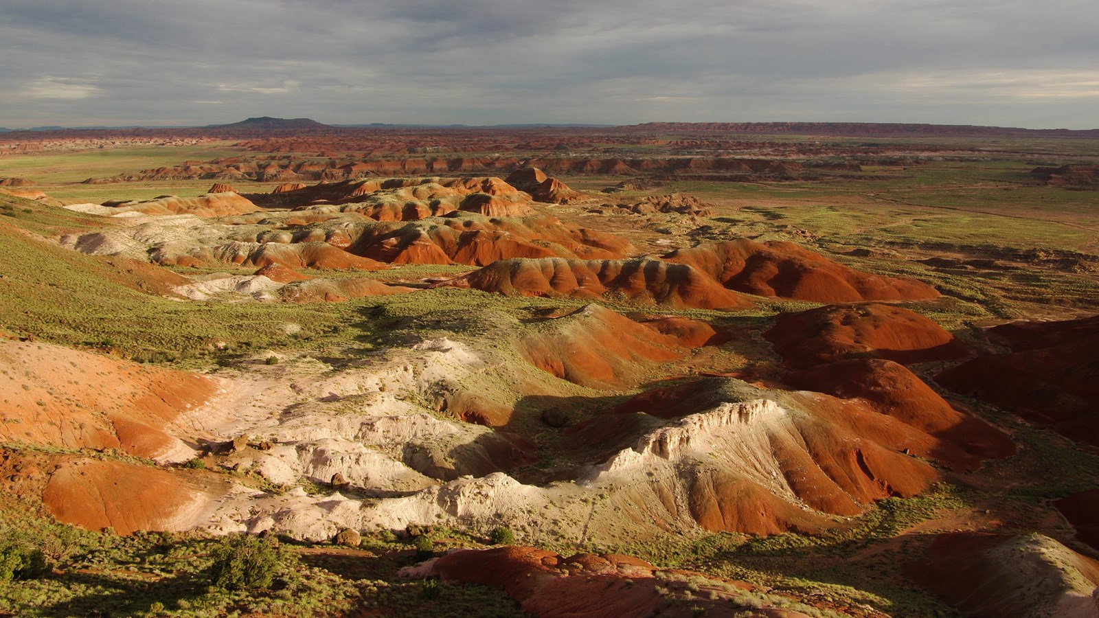 Red badland topography with highlights of sunlight under a cloudy sky.
